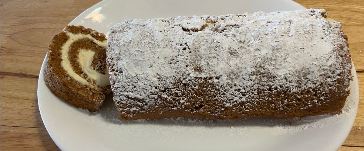 Pumpkin cream cheese roll dusted with powdered sugar with a slice on the left