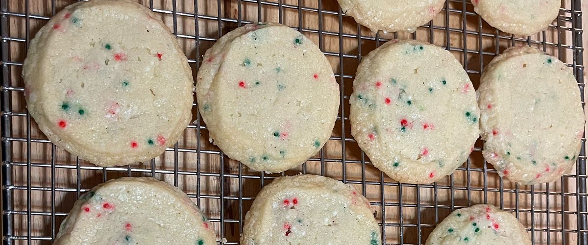 A dozen butter cookies with nonpareils with focus on four on cooling rack.