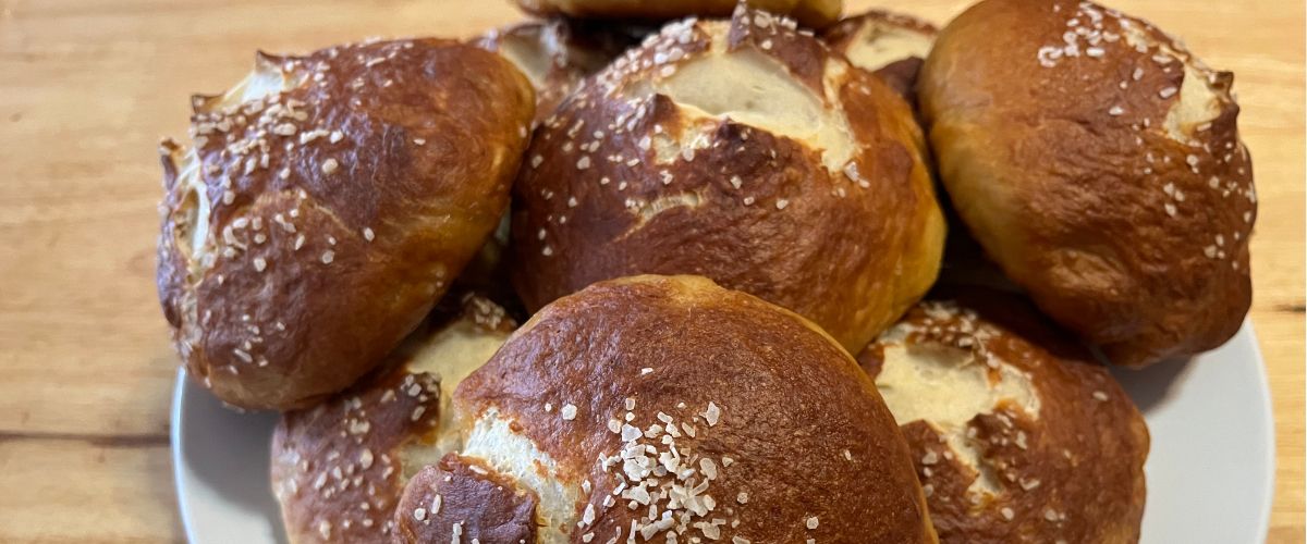 close up of pretzel buns on a white plate on a wood countertop