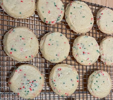 A dozen butter cookies with nonpareils on cooling rack.