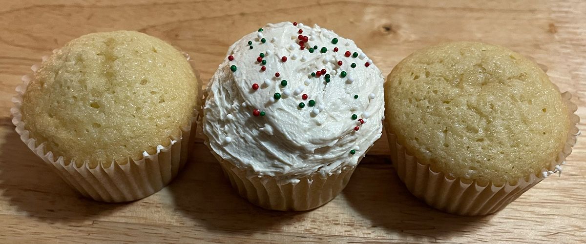 One frosted with nonpareils and two unfrosted vanilla cupcakes