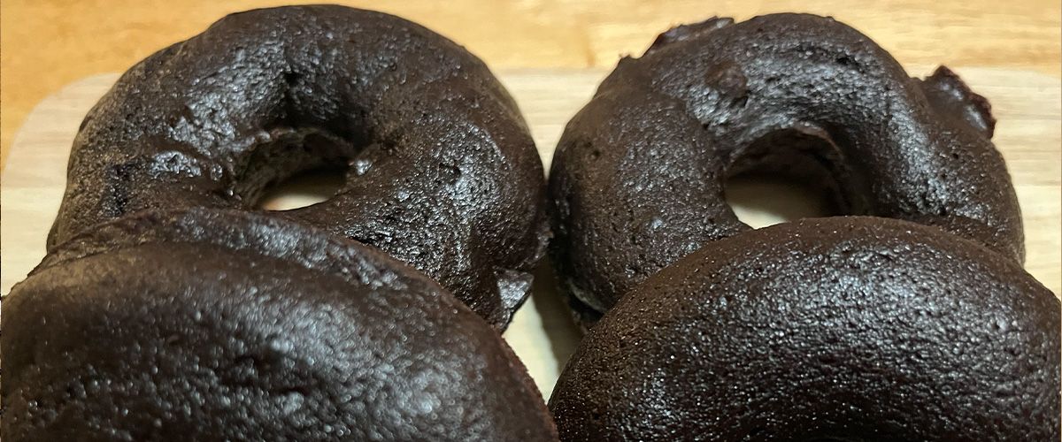 close up of four baked chocolate donuts, two foreground and two lying flat