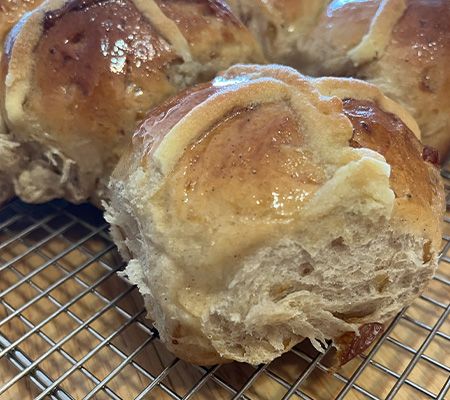 Close up of single hot cross bun on a cooling rack with others behind it