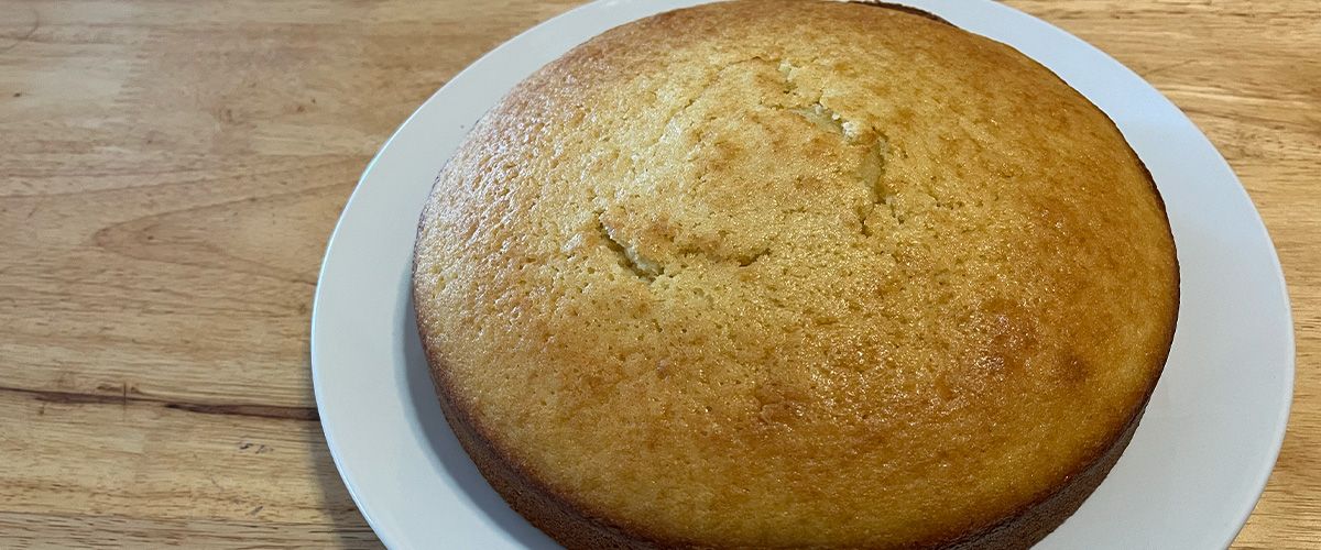 single layer olive oil cake on a white plate on wooden bench