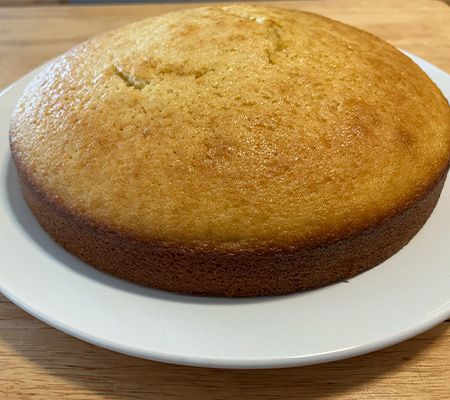 single layer olive oil cake on a white plate on wooden bench