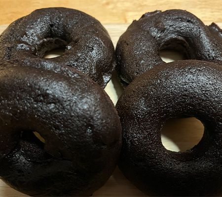 close up of four baked chocolate donuts, two foreground and two lying flat