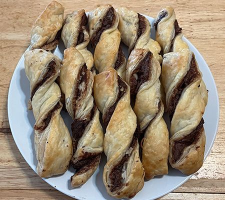 10 chocolate twists in two rows on a white plate on a wood cart