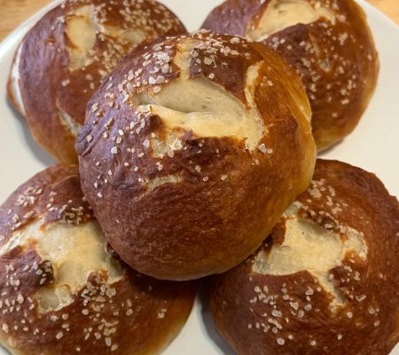 close up of pretzel buns on a white plate on a wood countertop